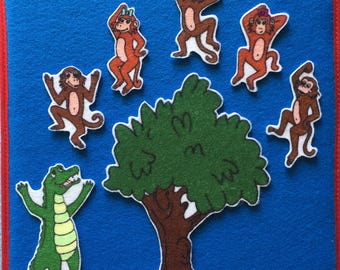 May include: A felt board with a green tree, a brown alligator, and five brown monkeys. The monkeys are in various poses, some with their arms raised and some with their arms down. The monkeys are all wearing different colored hats.