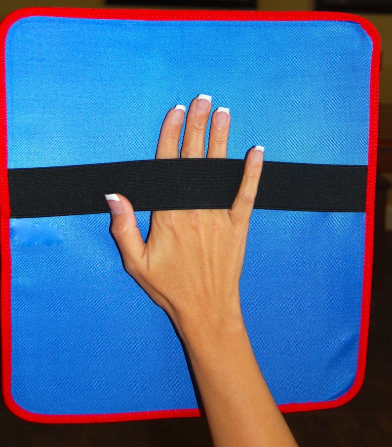 K&ouml;nnte beinhalten: Ein blaues rechteckiges Pad mit einem schwarzen Gummiband in der Mitte. Das Pad hat einen roten Rand.
