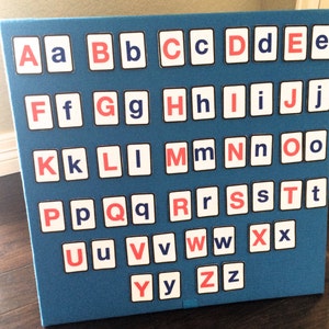 May include: A blue felt board with white and red letters of the alphabet. The letters are arranged in alphabetical order. The letters are in a square shape with a black border.