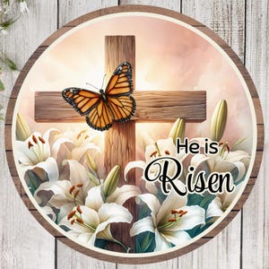 May include: A round wooden sign with a white cross and a butterfly. The cross is surrounded by white lilies and the text "He is Risen" is written in black.