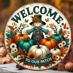 Könnte beinhalten: Rundes Holzschild mit dem Wort "WELCOME" in Türkis. Es zeigt eine Vogelscheuche, Kürbisse und den Text "TO OUR PATCH". Das Design umfasst Schmetterlinge, Blumen und Herbstblätter, die ein Herbstthema schaffen.