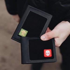 May include: Black leather wallet with a black interior and a square patch with a skull and crossbones design. The wallet is open, revealing the interior and a second patch with a skull design.