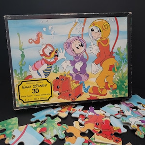 May include: A 30-piece Walt Disney jigsaw puzzle featuring Mickey Mouse, Donald Duck, and Goofy dressed as scuba divers. The puzzle box shows the characters underwater with a treasure chest and a seahorse.