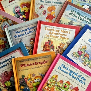 May include: A selection of children's books featuring the Fraggle Rock characters. Titles include "Best Friends," "The Cave of the Lost Fraggle," and "What's a Fraggle?" The covers are brightly coloured and feature illustrations of the characters.