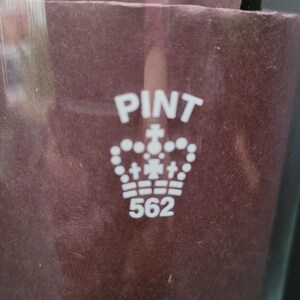 May include: A white glass pint glass with the words "PINT" and "562" printed on it. A crown with crosses is printed between the words.