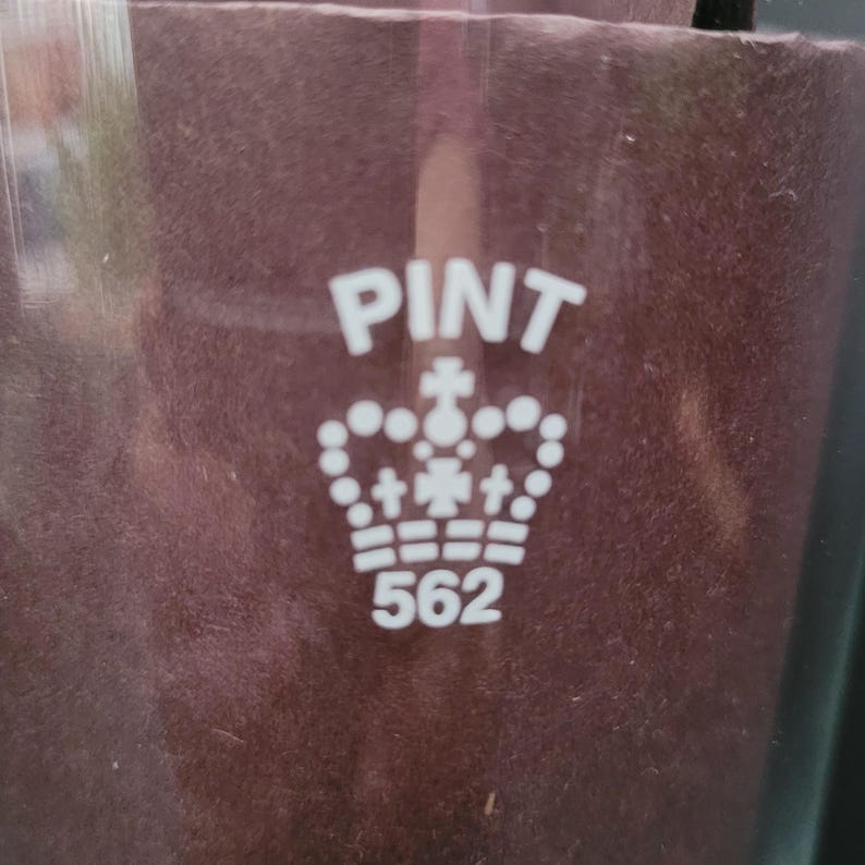 May include: A white glass pint glass with the words "PINT" and "562" printed on it. A crown with crosses is printed between the words.