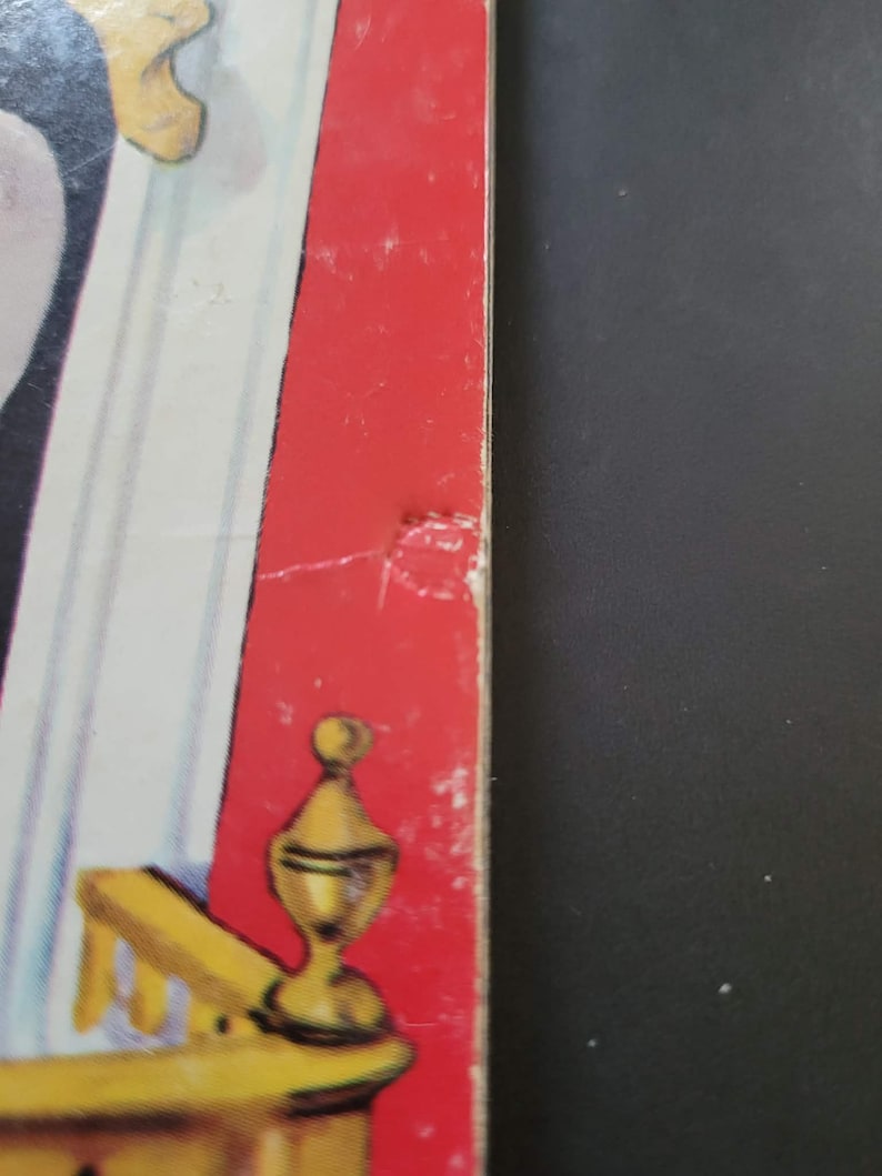 K&ouml;nnte beinhalten: Ein Abschnitt eines Vintage-Buchcovers mit rotem Buchr&uuml;cken und einem Teil einer gelb-wei&szlig;en Illustration. Der Buchr&uuml;cken weist einige Abnutzungserscheinungen auf. Die Illustration zeigt ein goldfarbenes dekoratives Element.