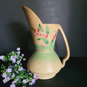 May include: A vintage ceramic pitcher with a green and beige glaze. The pitcher features a floral design with pink and green flowers.