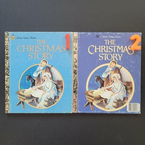 K&ouml;nnte beinhalten: Zwei Vintage "The Christmas Story" Little Golden B&uuml;cher. Die blauen Einb&auml;nde zeigen eine Illustration der Weihnachtsgeschichte. Ein Buch hat die rote Nummer 1, das andere die orangefarbene Nummer 2.