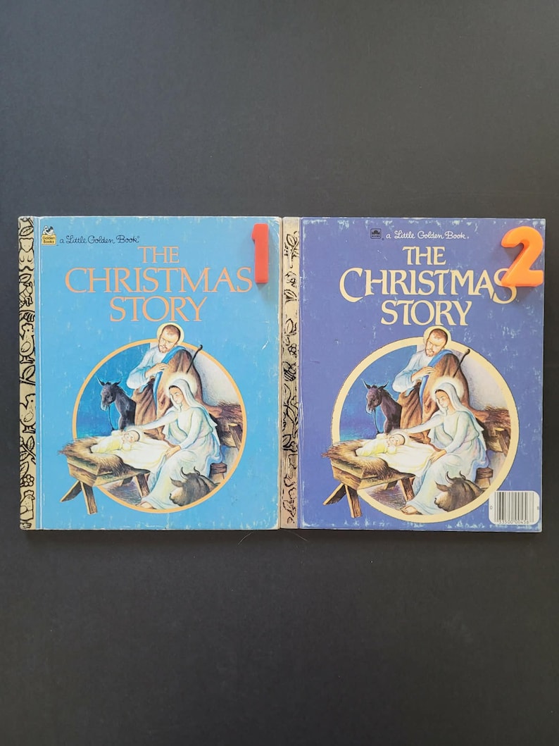 K&ouml;nnte beinhalten: Zwei Vintage "The Christmas Story" Little Golden B&uuml;cher. Die blauen Einb&auml;nde zeigen eine Illustration der Weihnachtsgeschichte. Ein Buch hat die rote Nummer 1, das andere die orangefarbene Nummer 2.