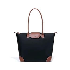 May include: Black tote bag with brown leather accents on the corners, flap, and handles. The bag has a rectangular shape with a zipper closure and a brown leather flap with a snap closure. The handles are long and brown.