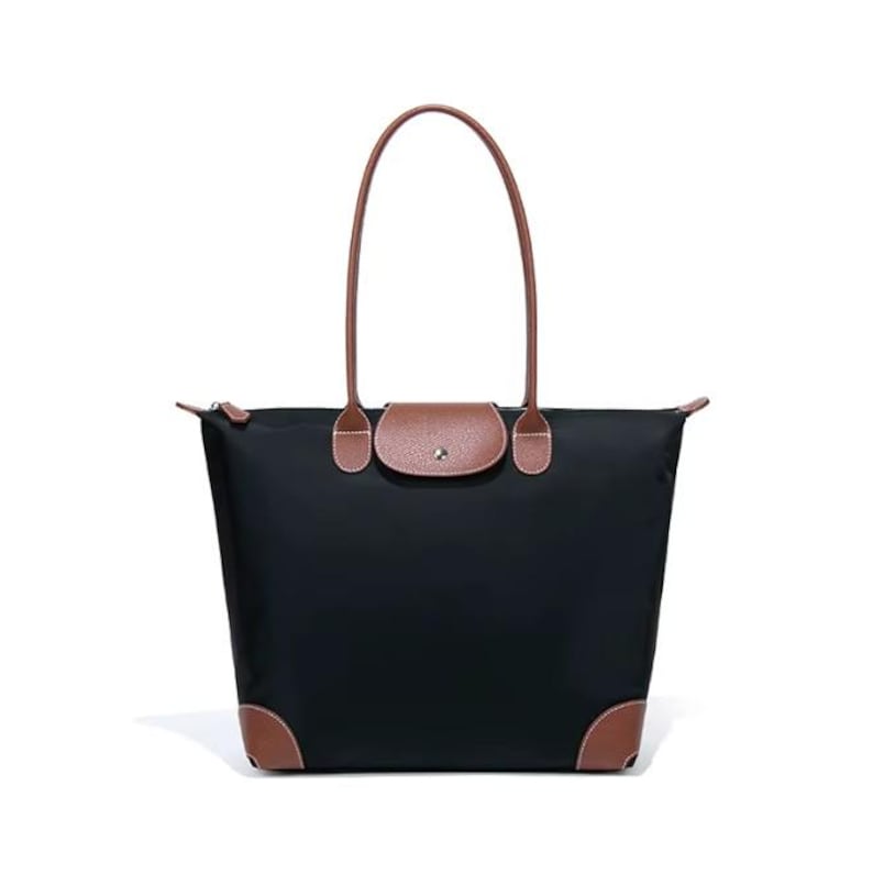 May include: Black tote bag with brown leather accents on the corners, flap, and handles. The bag has a rectangular shape with a zipper closure and a brown leather flap with a snap closure. The handles are long and brown.