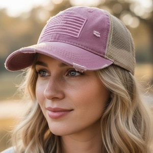 May include: A dusty rose baseball cap with a distressed American flag patch. The cap has a mesh back and a curved brim. The hat is a stylish accessory for casual wear, offering sun protection and a patriotic design.