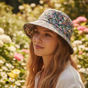 May include: A floral print bucket hat with a dark background and a wide brim. The hat features a pattern of pink, yellow, and purple flowers. The hat is worn outdoors in a garden setting.