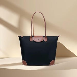 May include: A black tote bag with brown leather accents. The bag has a rectangular shape with a flap closure and two long handles. The corners of the bag are also reinforced with brown leather.
