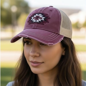 May include: A maroon baseball cap with a distressed brim and a tan mesh back. The cap features a geometric design in black, white, and maroon on the front. This hat is a stylish accessory for casual wear.