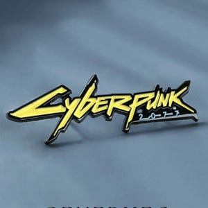 Könnte beinhalten: Ein gelber und schwarzer Cyberpunk 2077 Pin. Der Pin zeigt das Logo des Spiels mit dem Text "Cyberpunk 2077" in einer stilisierten Schriftart. Der Pin ist vor einem grauen Hintergrund platziert. Das Wort "GENERHEO" steht unten.