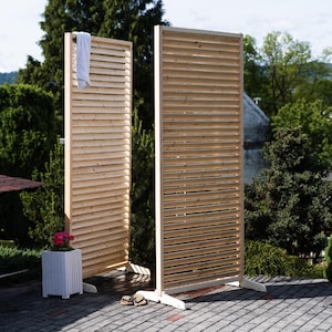 May include: Two wooden privacy screens with slatted panels. The screens are made of natural wood and are standing on a patio.