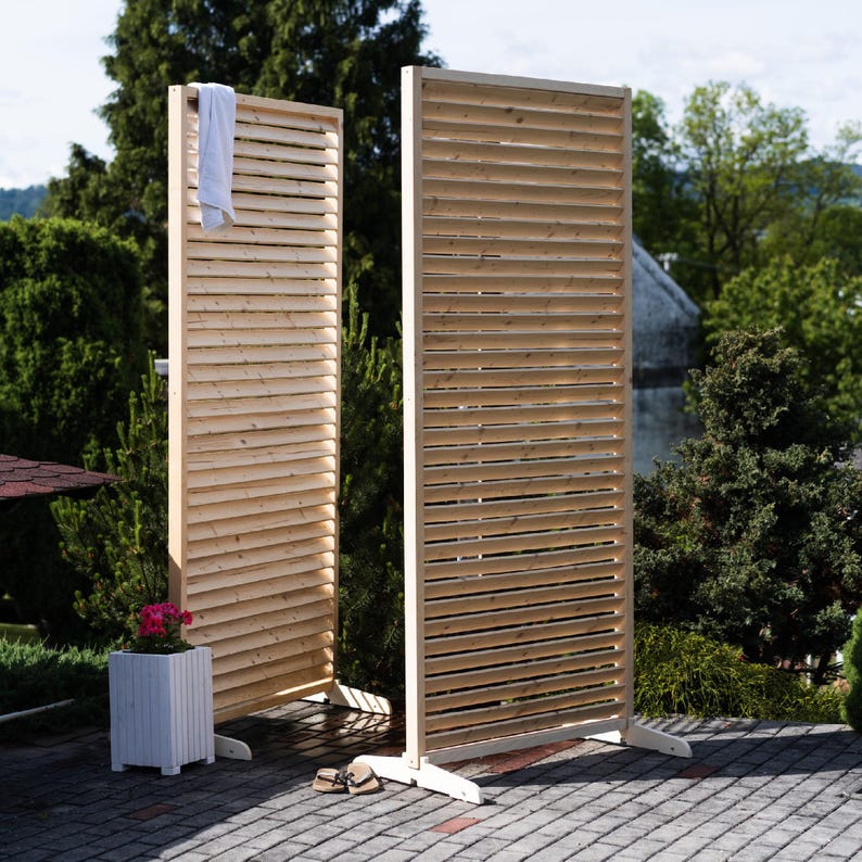 May include: Two wooden privacy screens with slatted panels. The screens are made of natural wood and are standing on a patio.