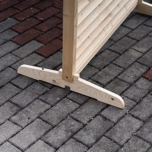 May include: A wooden room divider with a slatted design and a natural finish. The divider is standing on a gray brick patio.