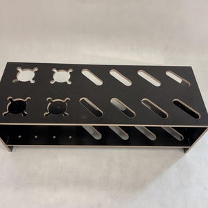 Può includere: Scaffale in legno nero a due livelli con più cerchi e ovali ritagliati. Lo scaffale è progettato per contenere oggetti come scarpe o altri oggetti.