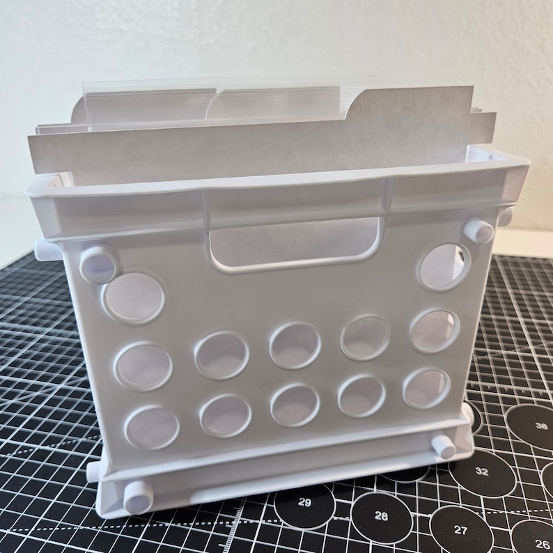 May include: White plastic storage crate with dividers and a handle. The crate has a grid pattern on the sides and a clear plastic insert for organizing items.