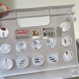 May include: White plastic Sterilite storage crate with a label that reads "9" L x 7 3/4" W x 6" H (22.9 cm x 19.7 cm x 15.6 cm)" and "Made in USA. Fabriqu&eacute; aux EU. Hecho en los EUA. 1005LABS - White".