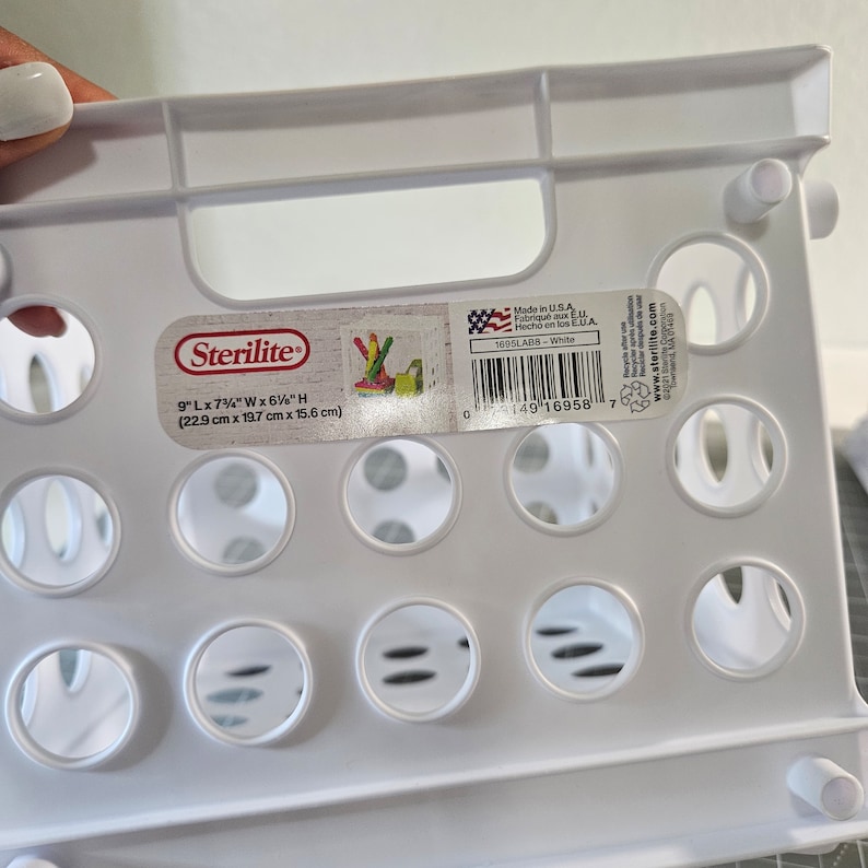 May include: White plastic Sterilite storage crate with a label that reads "9" L x 7 3/4" W x 6" H (22.9 cm x 19.7 cm x 15.6 cm)" and "Made in USA. Fabriqu&eacute; aux EU. Hecho en los EUA. 1005LABS - White".