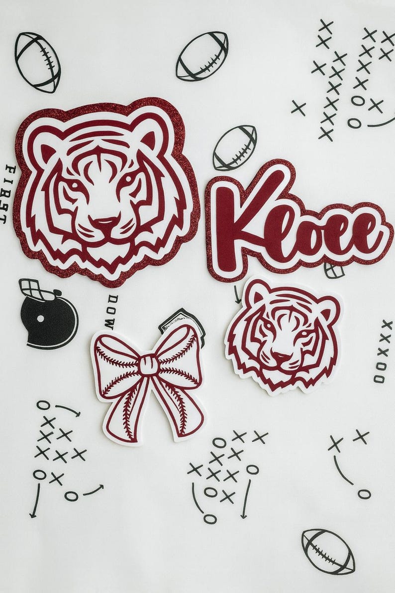May include: A selection of maroon and white sports-themed stickers and graphics. Features tiger head designs, the name "Kloee", American footballs, a baseball bow, and football play diagrams. The word "FIRST" is visible.