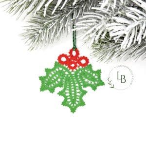 May include: A green and red crocheted holly leaf Christmas ornament. The ornament is made of green lace with red berries and is suspended from a green string. It hangs from a snow-covered evergreen branch. The text "Lacy Botanics" is visible.