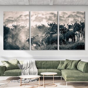 Triptych wall art featuring a herd of wildebeest in monochrome. The image showcases a large group of dark-colored wildebeest against a light, hazy background. The animals are captured in a dynamic pose, suggesting movement and interaction within the herd. The overall aesthetic is one of wildlife photography, suitable for nature or wildlife-themed decor.