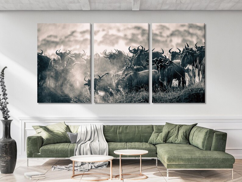 Triptych wall art featuring a herd of wildebeest in monochrome. The image showcases a large group of dark-colored wildebeest against a light, hazy background. The animals are captured in a dynamic pose, suggesting movement and interaction within the herd. The overall aesthetic is one of wildlife photography, suitable for nature or wildlife-themed decor.