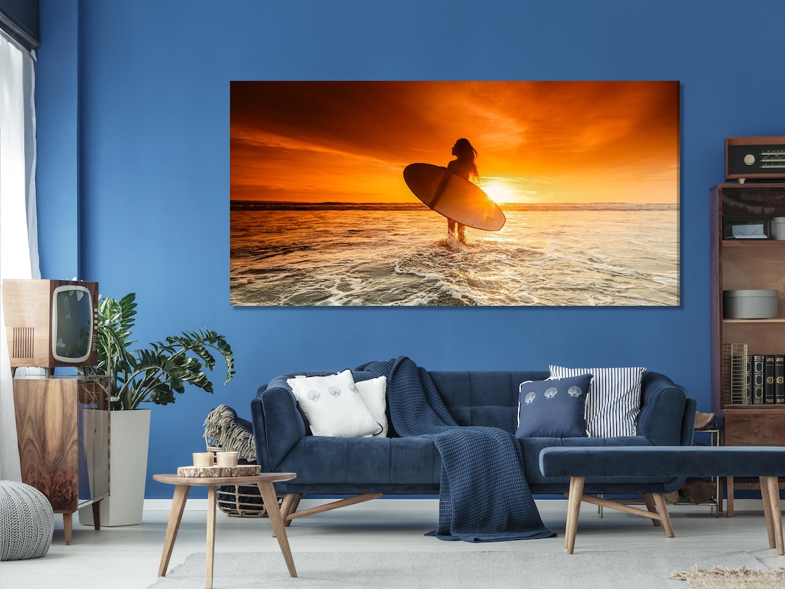 Sunset beach scene with a silhouetted surfer holding a surfboard in front of golden ocean waves detail view