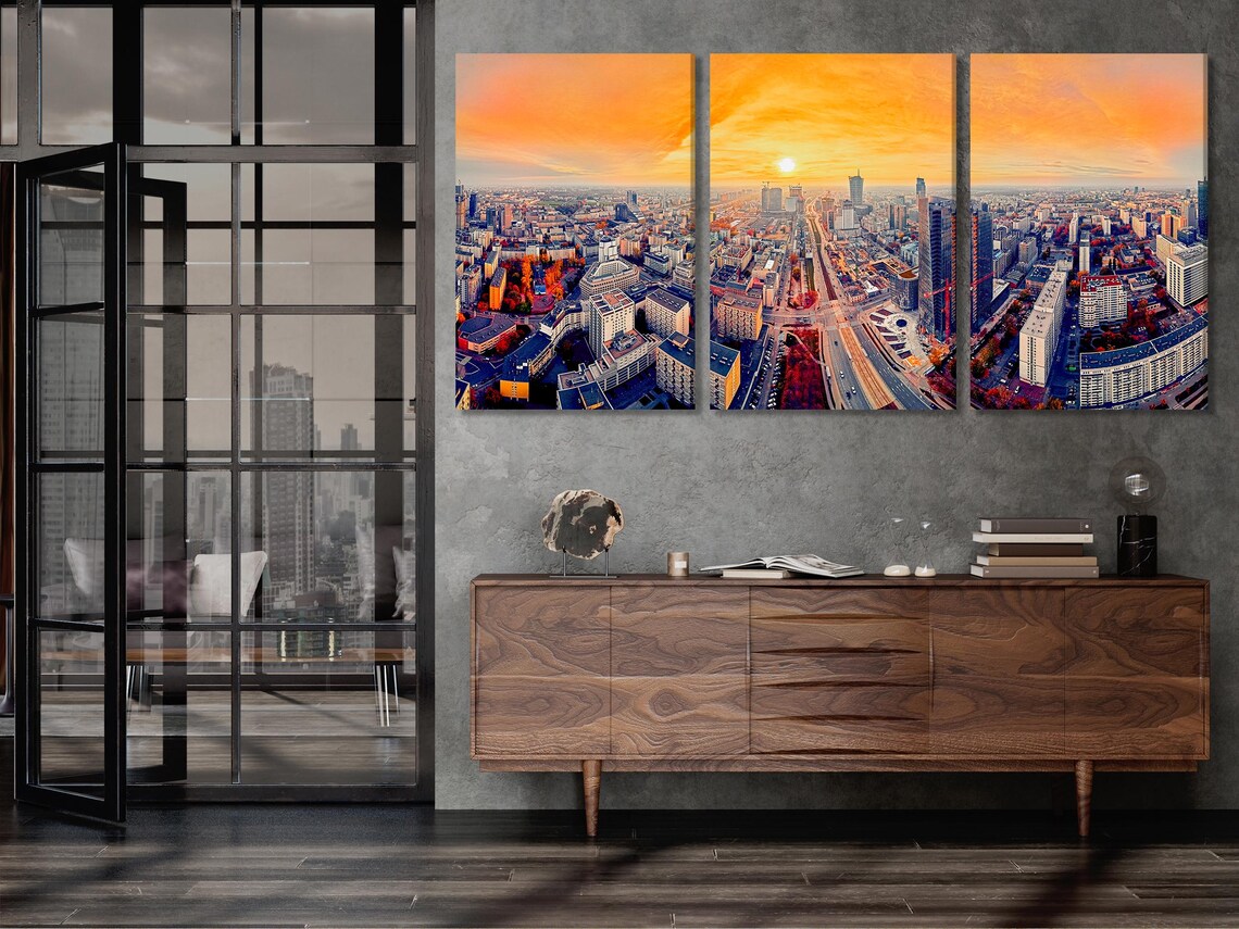 A panoramic city skyline at sunset shows tall buildings and a wide avenue cutting through the streets under a glowing orange sky detail view