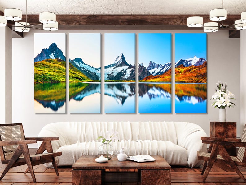 Mountain sunrise landscape with snow-capped peaks and mirrored lake reflection in blue, green and gold tones