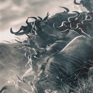 A monochrome photograph depicts a herd of wildebeest in motion. The animals are rendered in shades of gray, creating a dramatic, almost abstract effect. Their horns are prominent, and their forms blend together, suggesting a sense of movement and energy. The background is a hazy, light gray, providing a stark contrast to the darker tones of the wildebeest. The overall composition evokes a feeling of wildness and untamed nature.