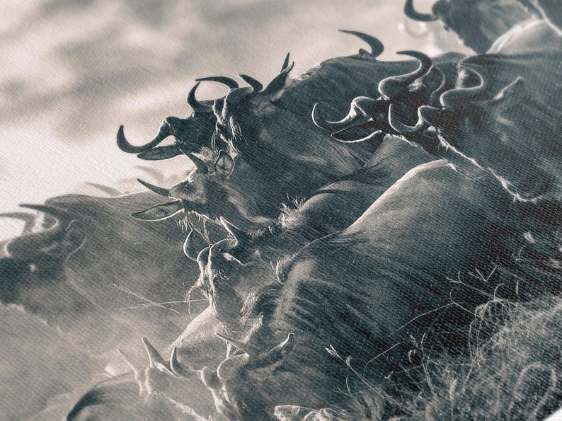 A monochrome photograph depicts a herd of wildebeest in motion. The animals are rendered in shades of gray, creating a dramatic, almost abstract effect. Their horns are prominent, and their forms blend together, suggesting a sense of movement and energy. The background is a hazy, light gray, providing a stark contrast to the darker tones of the wildebeest. The overall composition evokes a feeling of wildness and untamed nature.