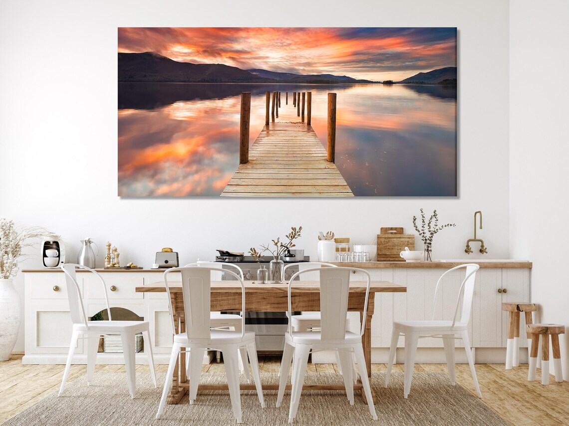 Dining table and chairs beneath three-panel lake sunset artwork on a light wall