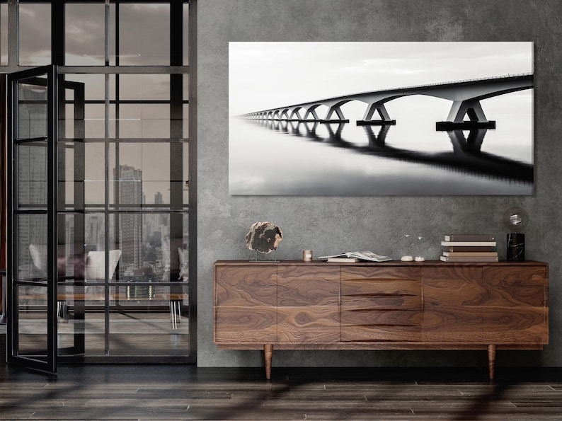 Black and white arched bridge spanning still water with reflections and a misty horizon