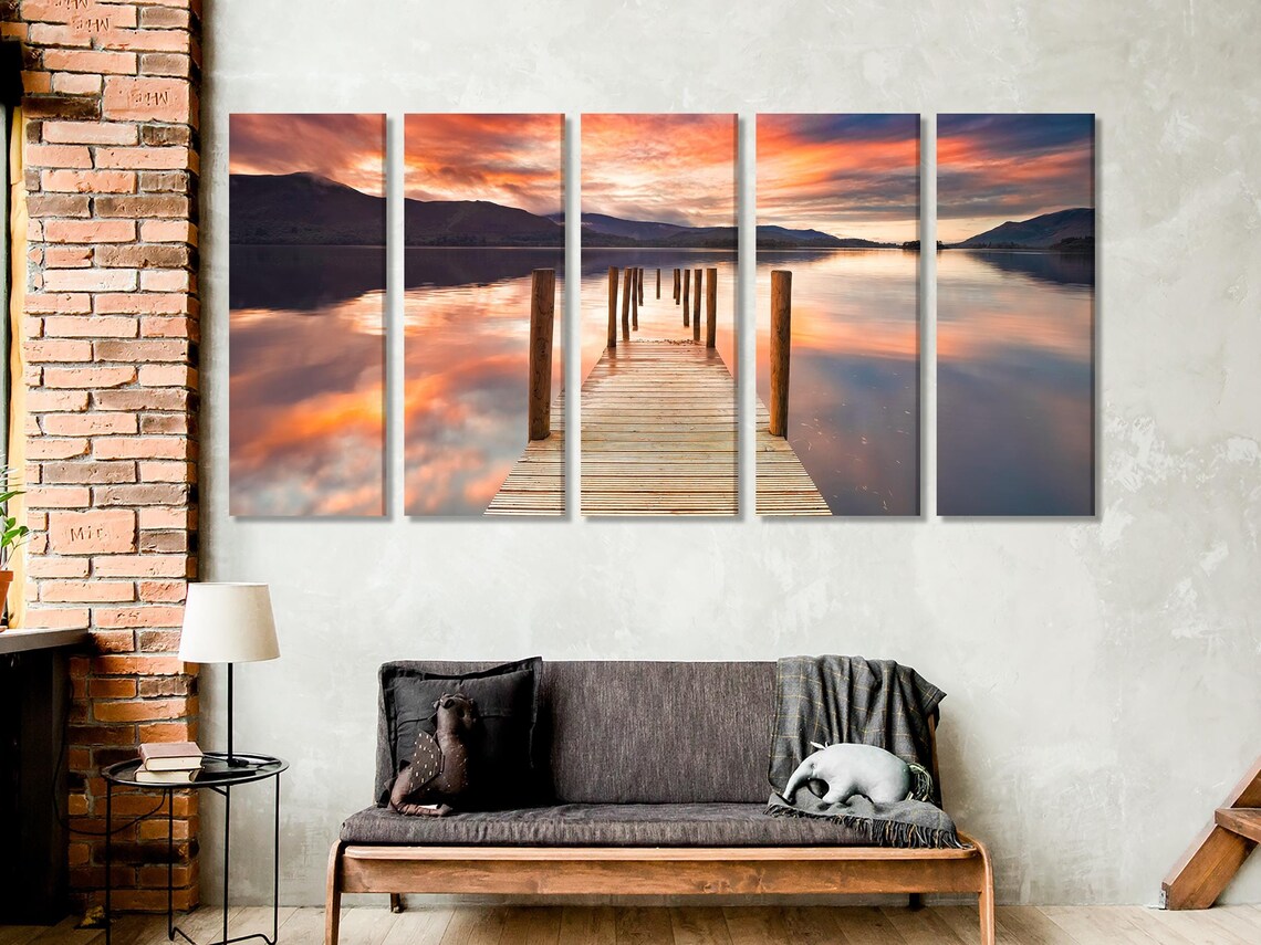 Dining table and chairs beneath three-panel lake sunset artwork on a light wall