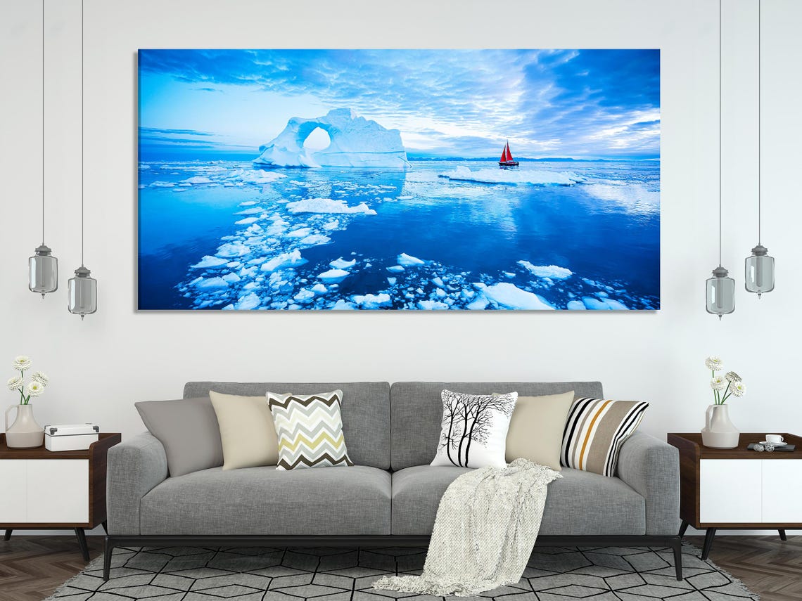 Arctic ocean seascape with icy iceberg arch shapes and a small red sailboat under a bright blue sky detail view