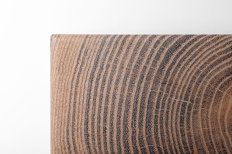 A rectangular piece of wood showing a cross-section of a tree trunk. The surface displays a series of concentric growth rings in alternating shades of dark brown and light tan, revealing the natural grain and texture of the timber.