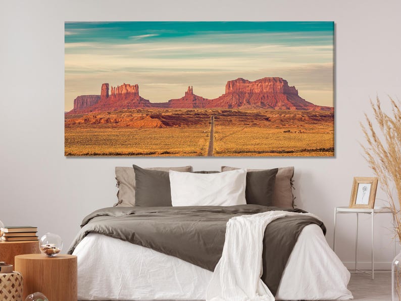 Panoramic desert landscape with a road leading to red rock buttes under a pale turquoise-tinted sky