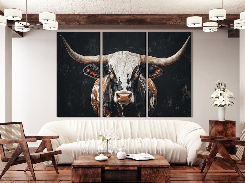 A three-panel artwork shows a longhorn-style cow portrait with sweeping horns against a dark, textured background, in high-contrast black, cream and