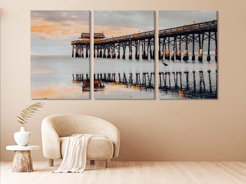 Coastal pier over calm water at sunset with reflections and a small bird on the posts