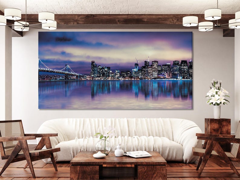 A night cityscape skyline glows in purples and blues, with a lit bridge, calm reflective water and a clouded sky