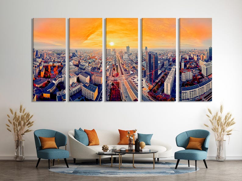 A panoramic city skyline at sunset shows tall buildings and a wide avenue cutting through the streets under a glowing orange sky