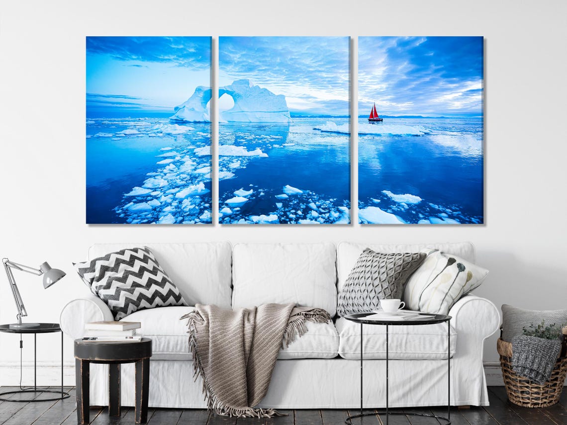 Arctic ocean seascape with icy iceberg arch shapes and a small red sailboat under a bright blue sky detail view