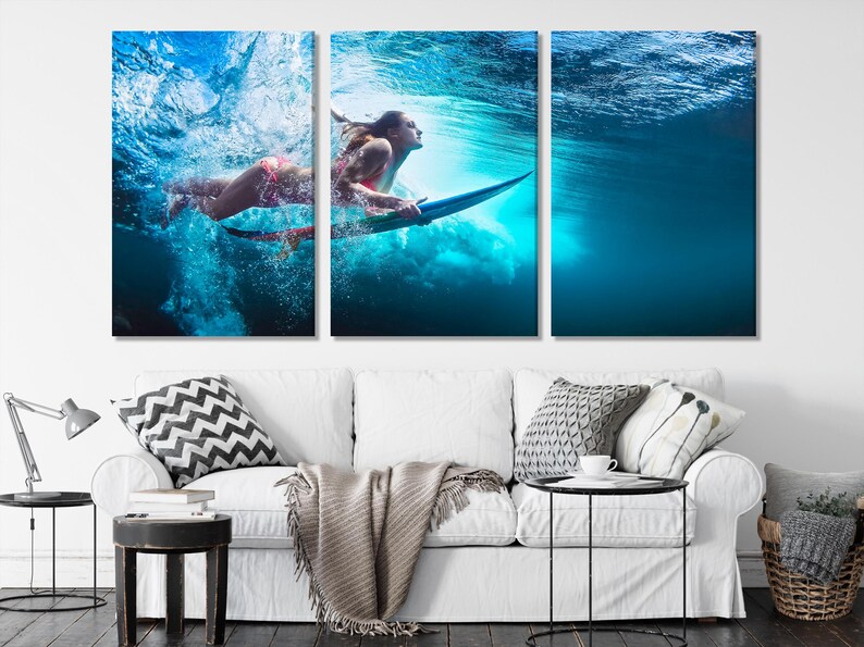 A three-panel triptych canvas print depicting a surfer underwater. The vibrant blue water is filled with bubbles and light. The surfer is positioned dynamically, creating a sense of motion and energy. The artwork features a woman in a bikini, surfing on a surfboard. The colors are predominantly blues and greens, with hints of pink from the surfer's attire. This artwork is perfect for adding a coastal vibe to any living space.