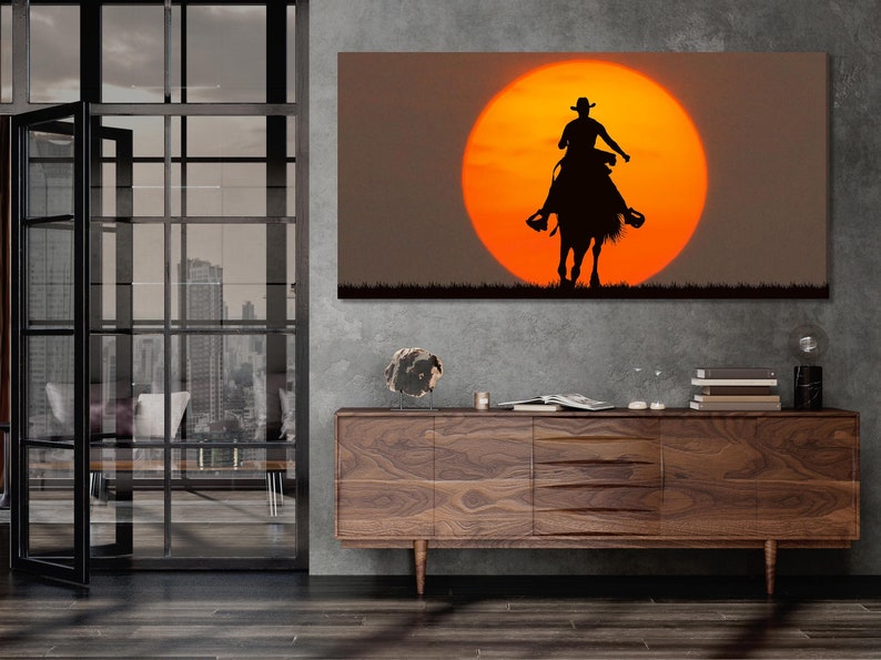 Black cowboy riding a horse silhouette beneath a glowing orange sun with dark grass